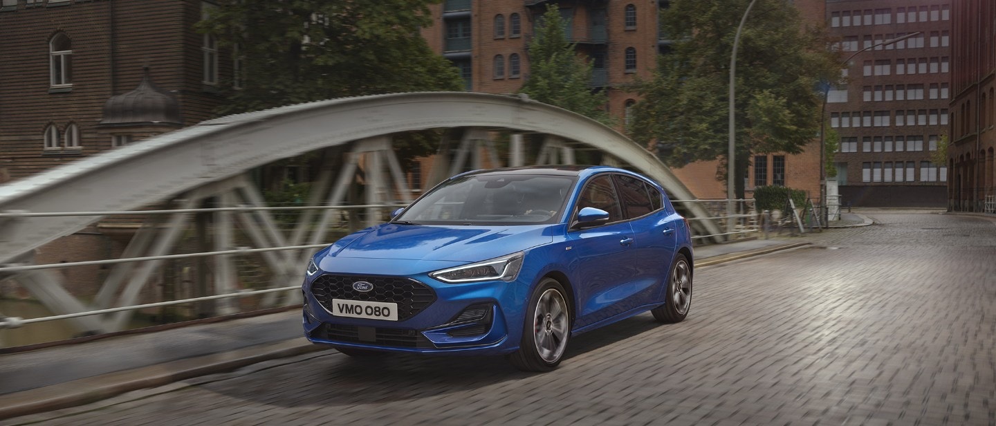 Ford Focus in Blau. Dreiviertelansicht, fährt auf einer Brücke