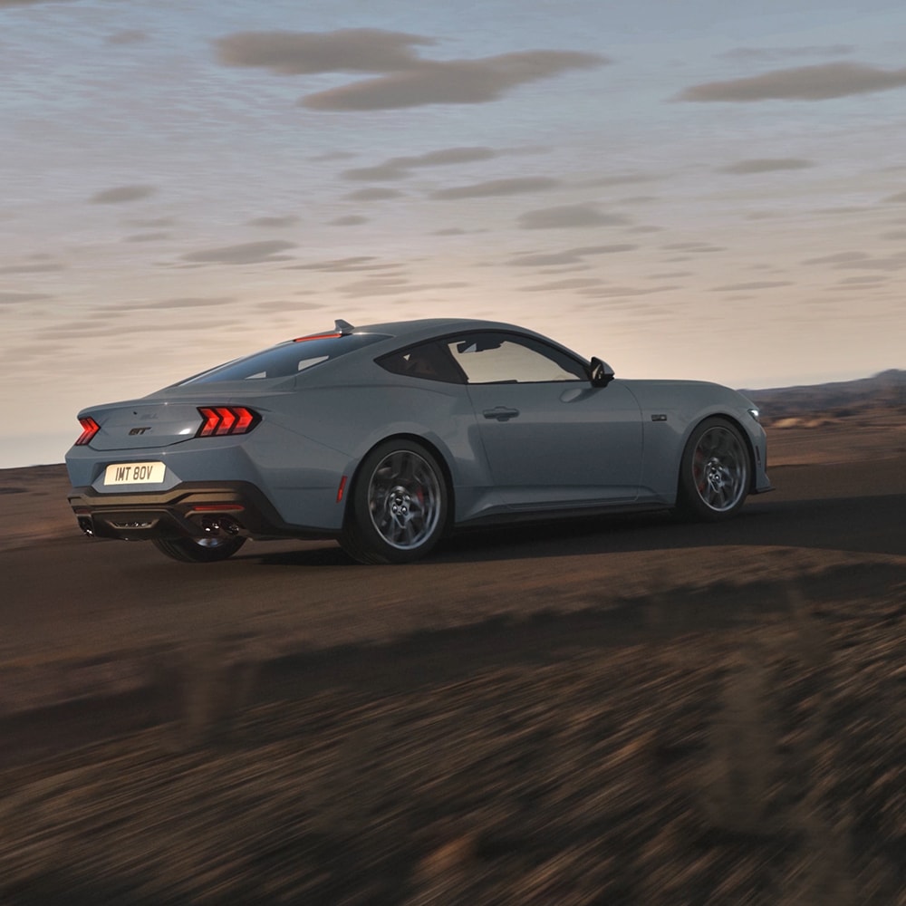 Ford Mustang in Blau. Dreiviertelansicht, fahrend auf einer unbefestigten Straße bei Sonnenuntergang.