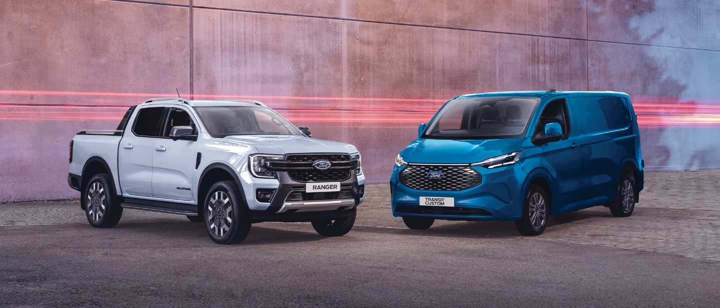 Ford Ranger PHEV in Weiß und Ford Transit Custom in Blau. Dreiviertelansicht, geparkt vor einer Mauer.