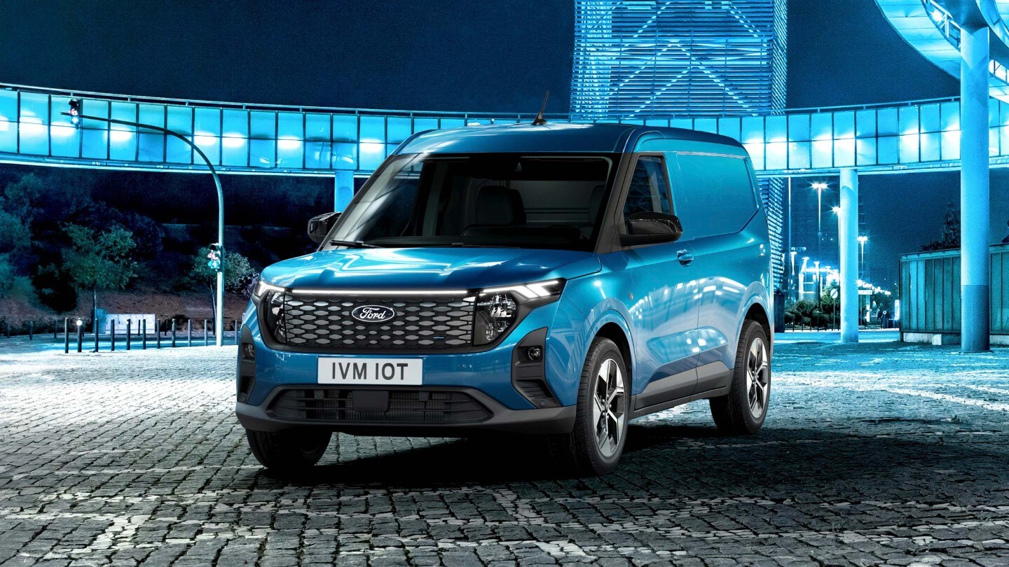 Ford E-Transit Courier in Blau. Dreiviertelansicht, stehend vor einer Garage bei Nacht.