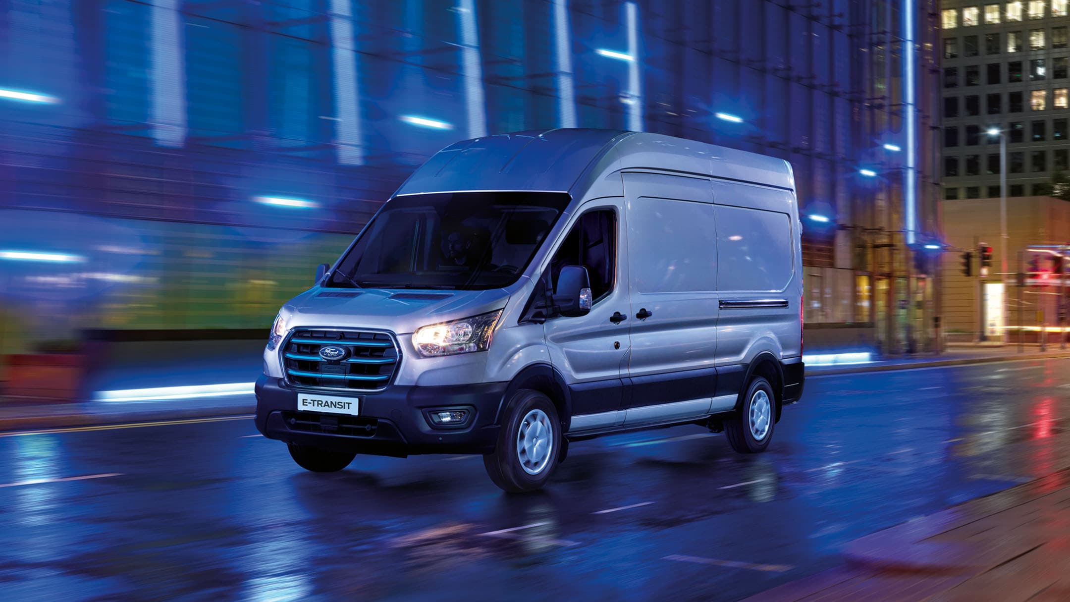 Ford E-Transit in Silber. Dreiviertelansicht, fahrend bei Nacht