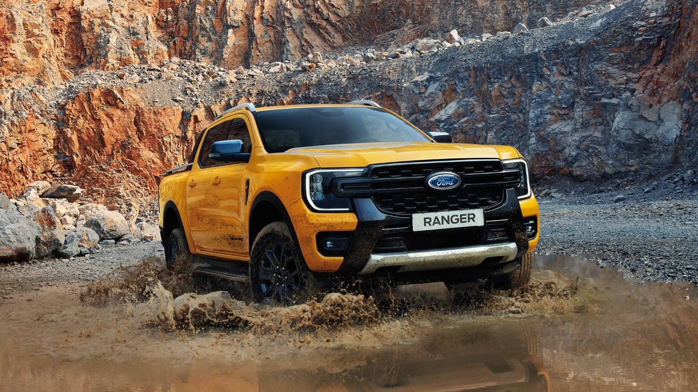 Ford Ranger in Orange. Dreiviertelansicht, fährt durch eine Wasserlacke
