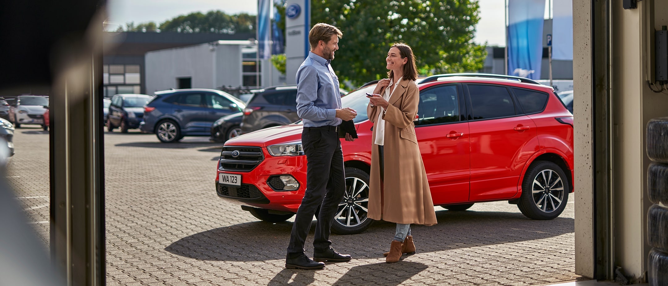 Vorderansicht eines roten Ford Kuga, mit zwei Personen, die sich daneben in einem Autohaus unterhalten.