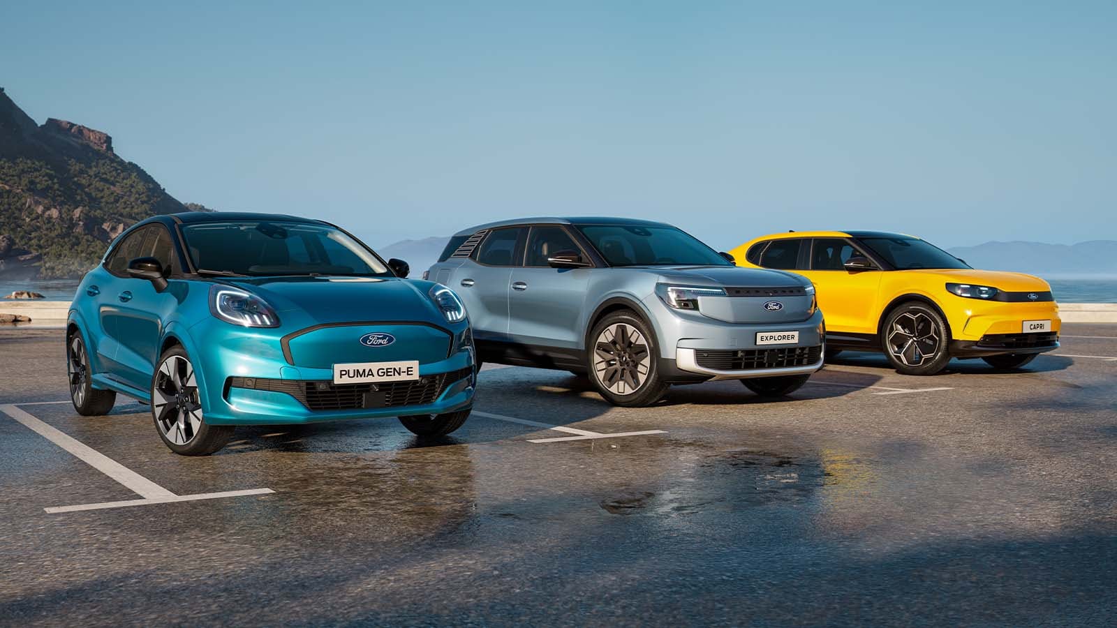 Ford Puma Gen-E, Explorer und Capri stehen auf einem Parkplatz. Im Hintergrund sieht man einen See mit Bergen.
