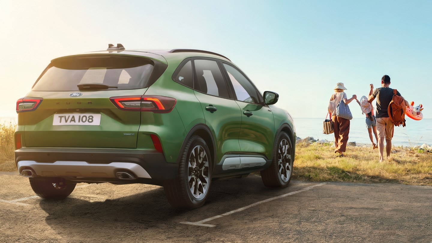 Eine lächelnde Frau lädt ihren Rucksack in den Kofferraum Ihres Ford, der in einer Winterlandschaft geparkt ist