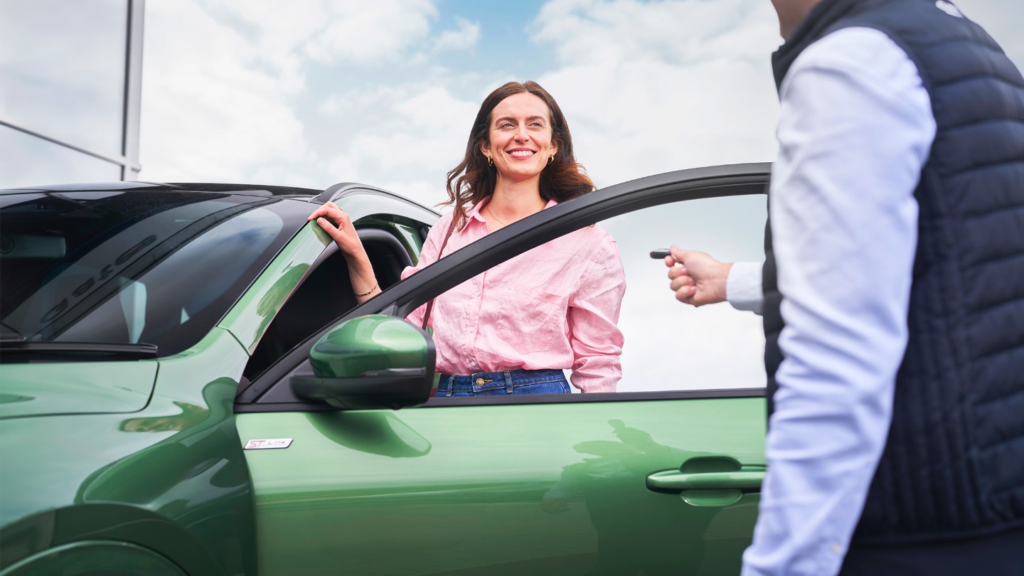 Eine lächelnde Frau lädt ihren Rucksack in den Kofferraum Ihres Ford, der in einer Winterlandschaft geparkt ist