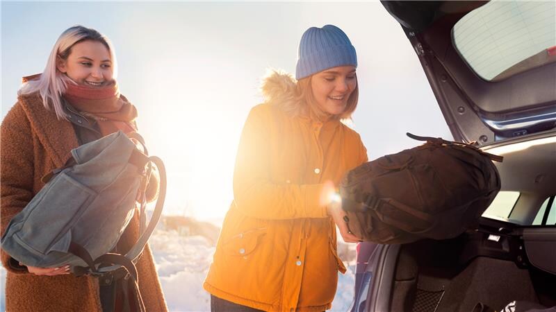 Eine lächelnde Frau lädt ihren Rucksack in den Kofferraum Ihres Ford, der in einer Winterlandschaft geparkt ist