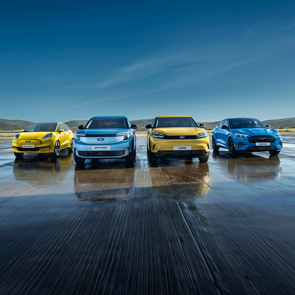 Puma Gen-E, Explorer, Capri und Mustang Mach-E stehen auf einer nassen Fahrbahn. Frontansicht der Fahrzeuge.