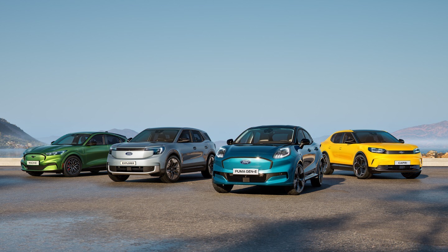 Ford Mustang Mach-E, Explorer, Puma Gen-E und Capri stehen nebeneinander auf einer nassen Fahrbahn mit Hügeln im Hintergrund.