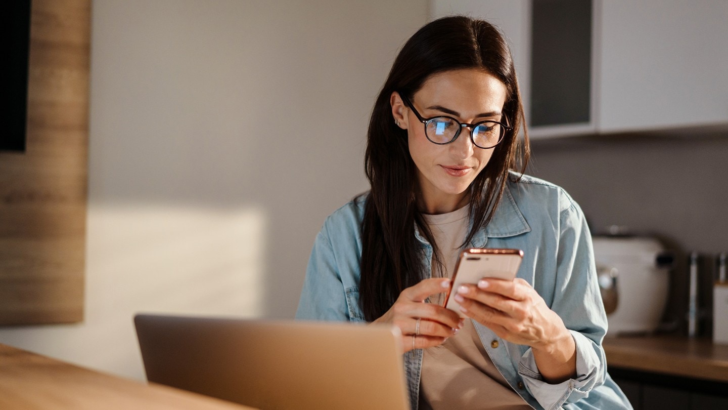 Person sitzt in einer Küche mit Laptop, hält ein Handy in der Hand und bucht einen Ford Service Termin online.
