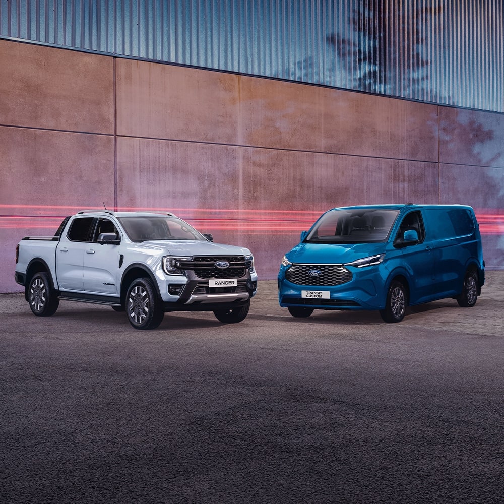 Ford Ranger PHEV in Weiß und Ford E-Transit Custom in Blau. Dreiviertelansicht, geparkt vor einer Mauer.