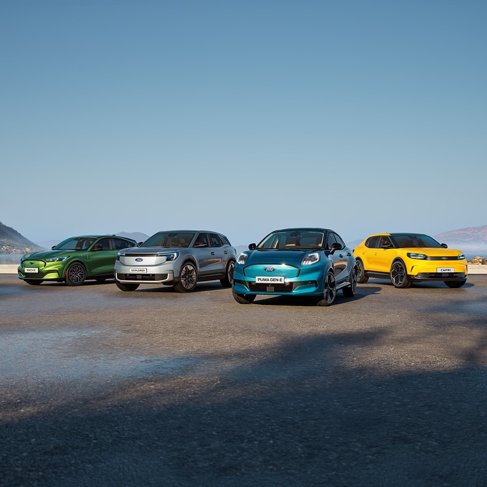 Puma Gen-E, Explorer, Capri und Mustang Mach-E stehen auf einer nassen Fahrbahn. Frontansicht der Fahrzeuge. 