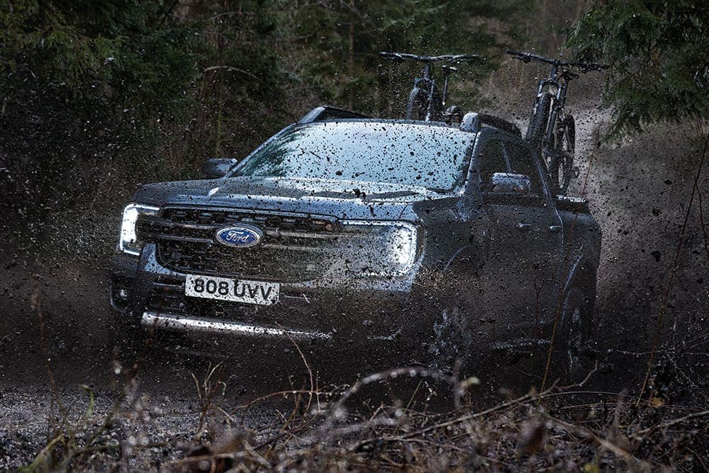 Ford Ranger in Grau. Dreiviertelansicht, fährt auf einem Offroad-Gelände durch Schlamm.