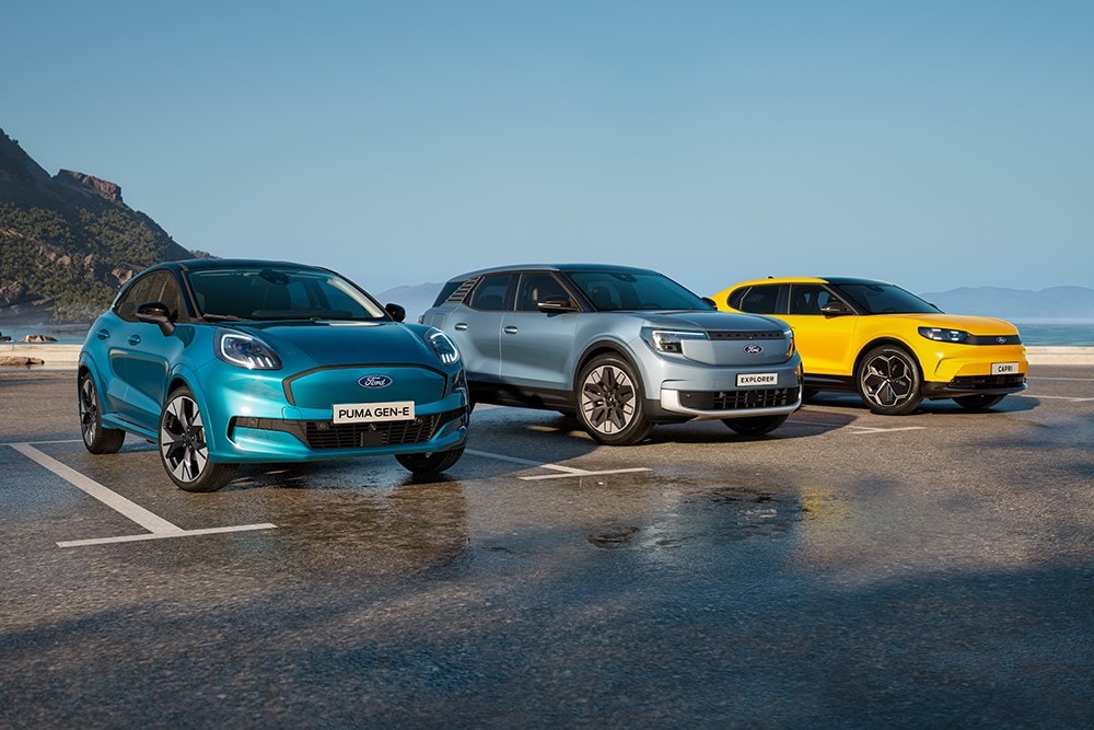 Puma Gen-E, Explorer, Capri und Mustang Mach-E stehen auf einer nassen Fahrbahn. Frontansicht der Fahrzeuge. 
