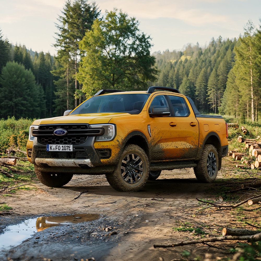 Ford Ranger in Orange mit Schlammspuren. Dreiviertelansicht, geparkt in einem Wald.
