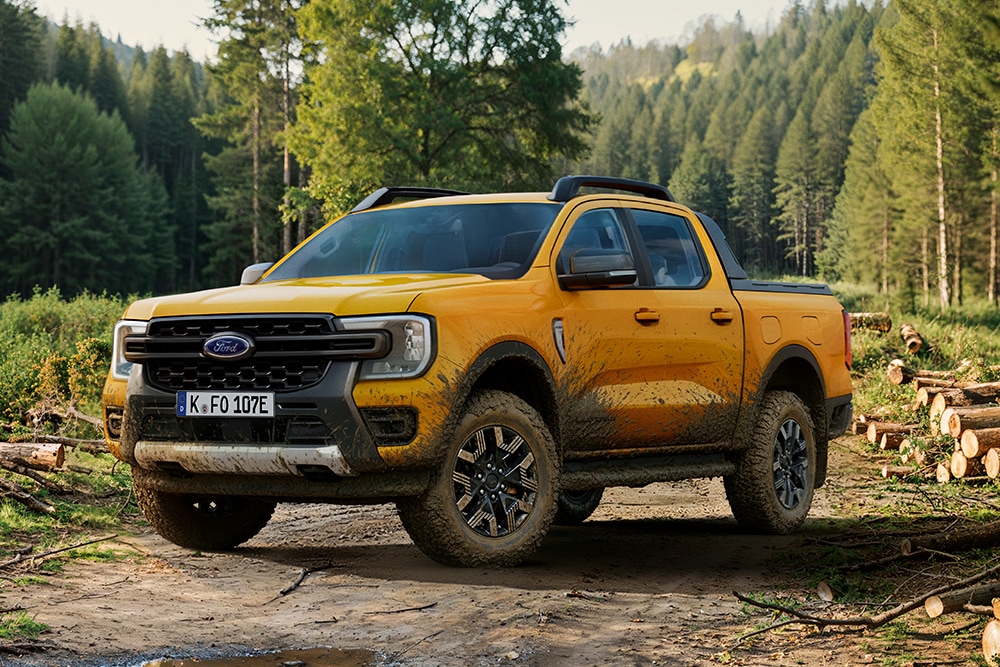Ford Ranger in Gelb mit Schlammspuren. Dreiviertelansicht, geparkt in einem Wald.