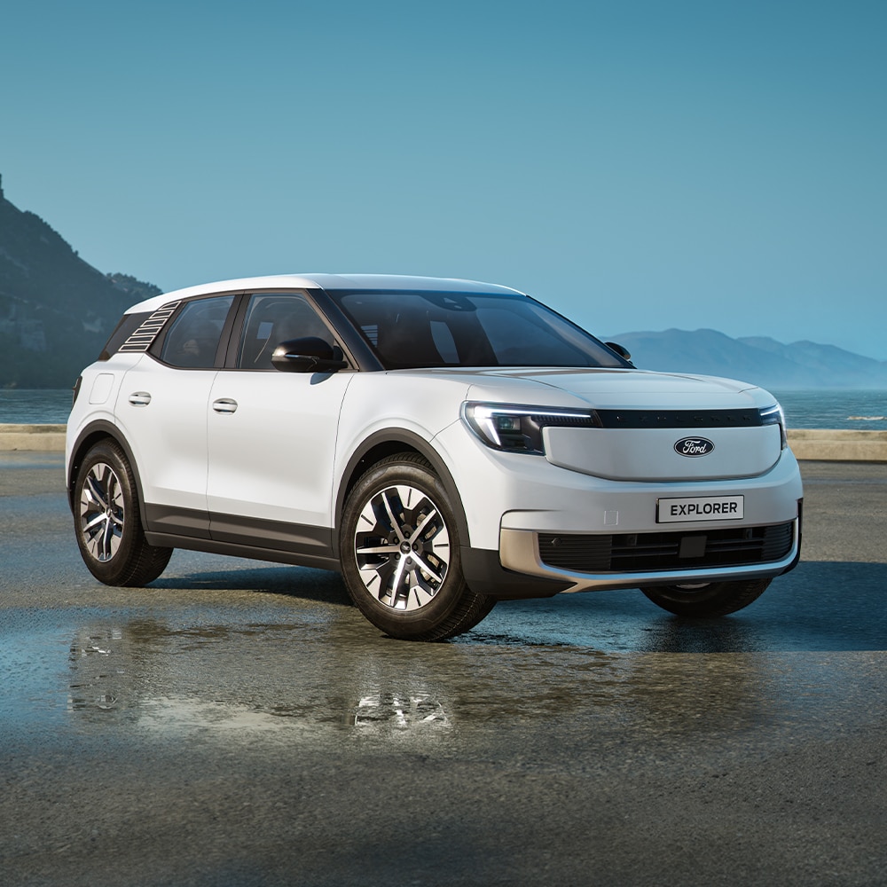 Ford Explorer in Weiß. Dreiviertelansicht, parkt auf einer nassen Fahrbahn mit Hügellandschaft im Hintergrund. 