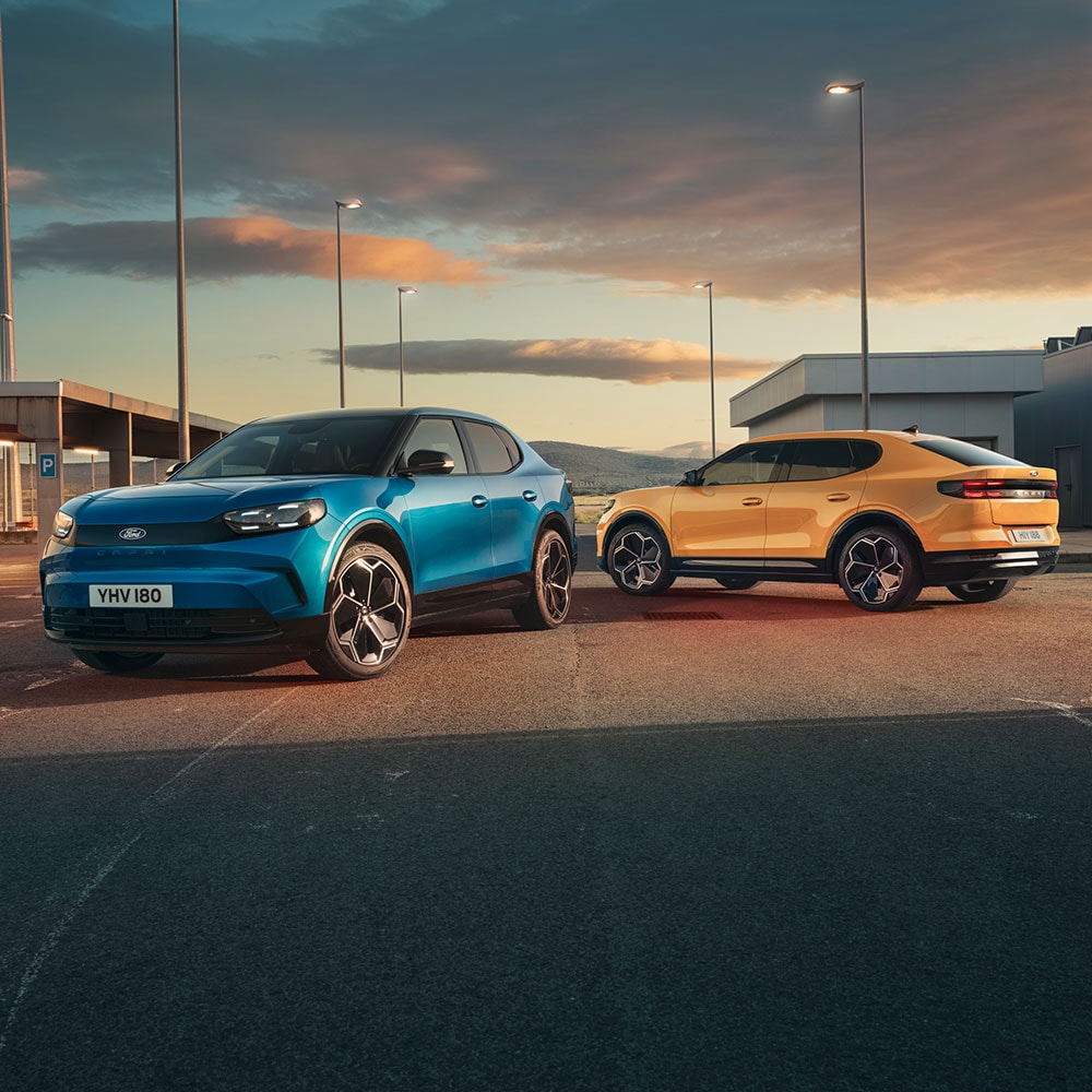 Ford Capri in Blau und Gelb. Die Fahrzeuge parken nebeneinander bei Sonnenuntergang auf einem öffentlichen Parkplatz.