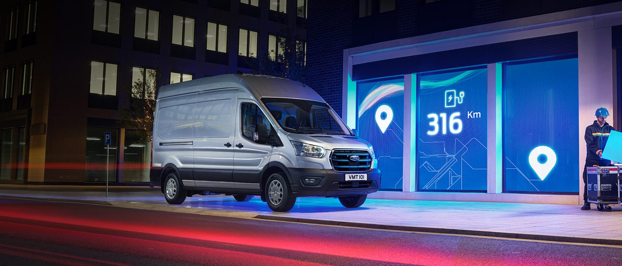 Ford E-Transit in Silber. Dreiviertelansicht, in einer Stadt bei Nacht