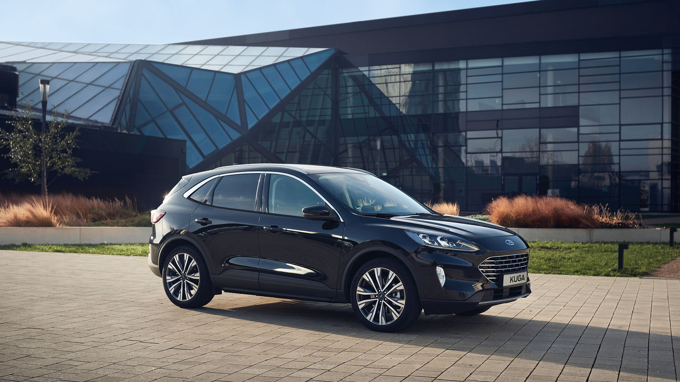 Ford Kuga in Schwarz. Dreiviertelansicht, parkt vor einem modernen Glasgebäude.