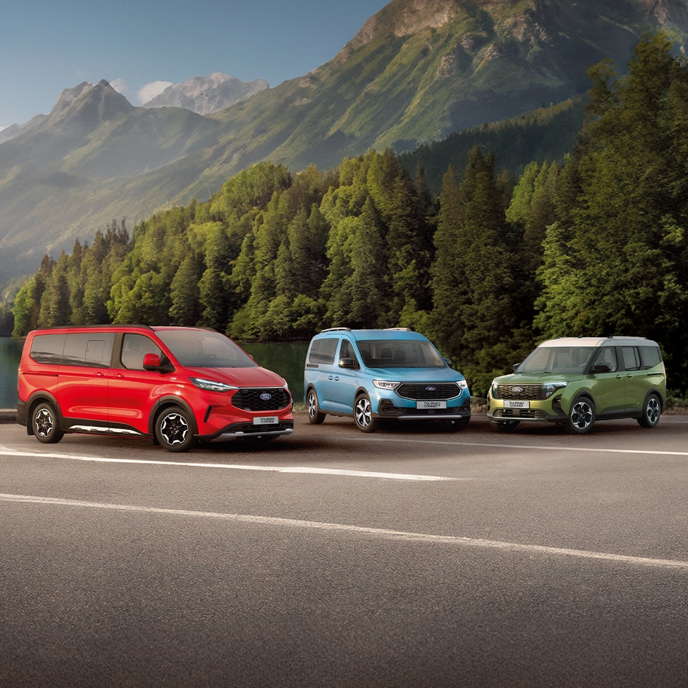 Ein roter Ford Tourneo Custom, ein blauer Tourneo Connect und ein grüner Tourneo Courier stehen nebeneinander auf einem Parkplatz, im Hintergrund ein grüner Wald.