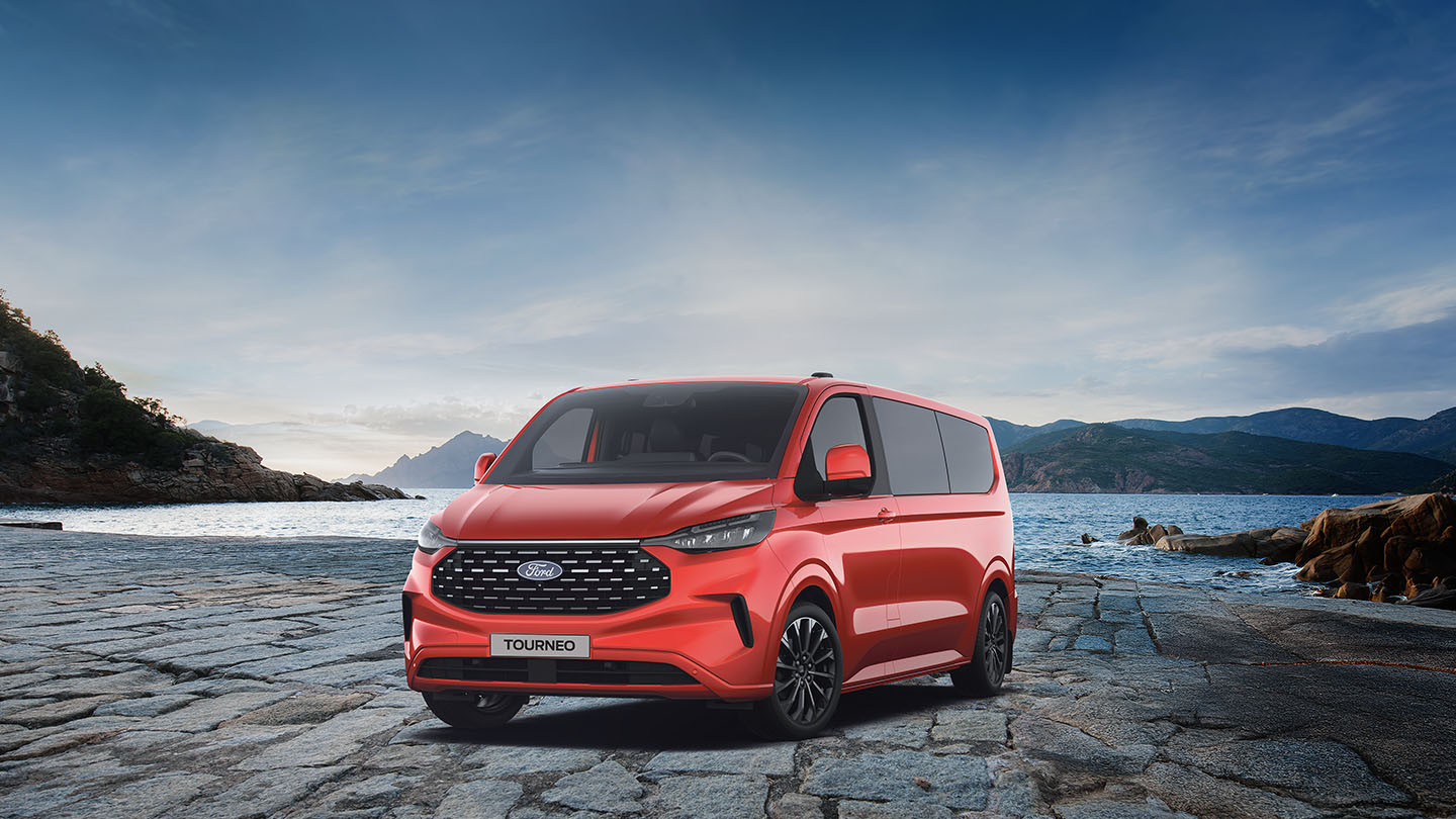 Ford Tourneo Custom in Rot. Dreiviertansicht, parkt vor einem See mit Berglandschaft.