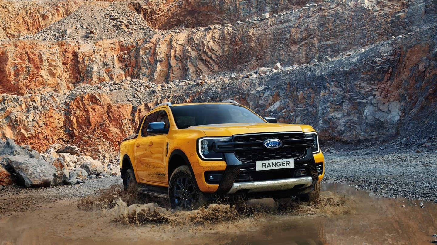 Ford Ranger in Orange. Dreiviertelansicht, fährt durch eine Wasserlache.