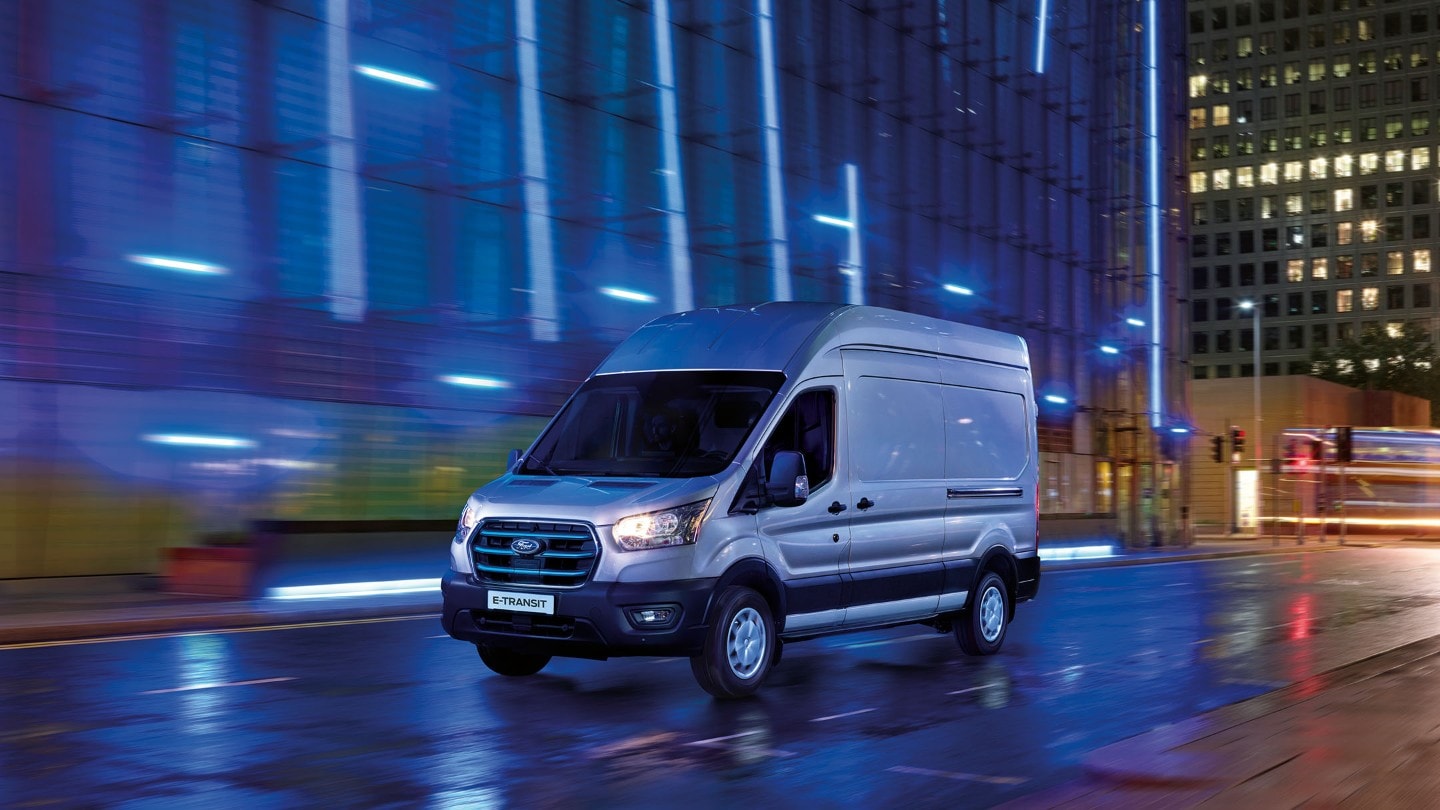 Ford E-Transit in Silber. Dreiviertelansicht, fährt bei Nacht.