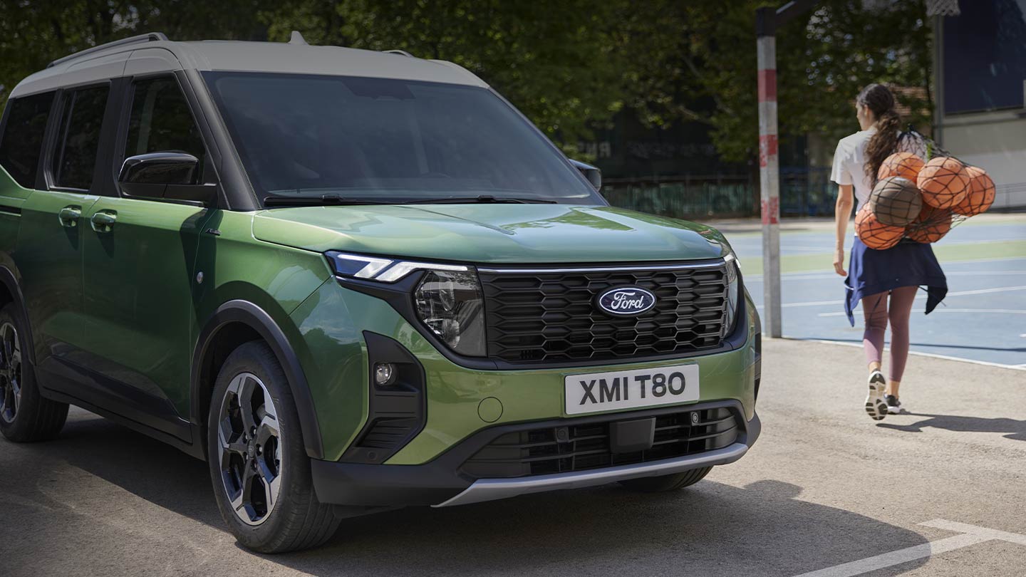 Ford Tourneo Courier in Grün. Dreiviertelansicht, parkt vor einem Basketballplatz. Daneben eine Person mit einem Ballnetz.
