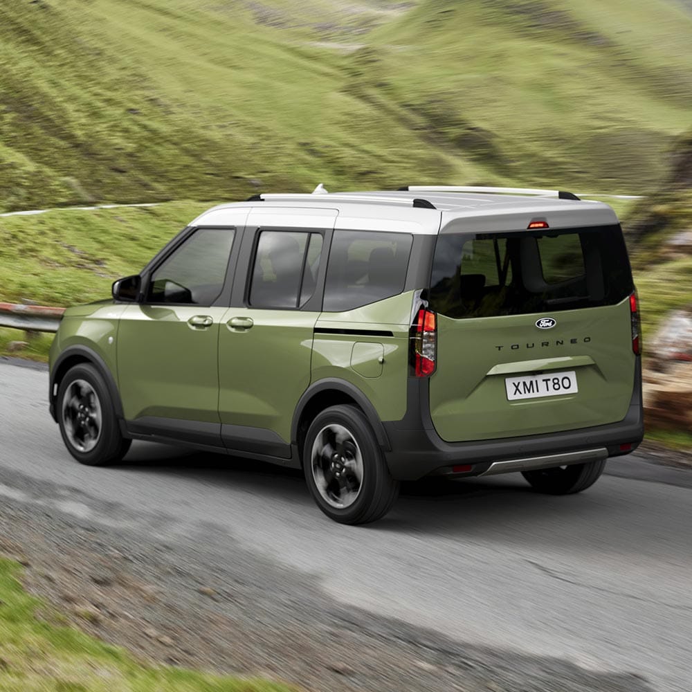 Ford Tourneo Courier in Grün. Dreiviertelansicht, fahrend auf einer Straße mit Landschaft im Hintergrund.