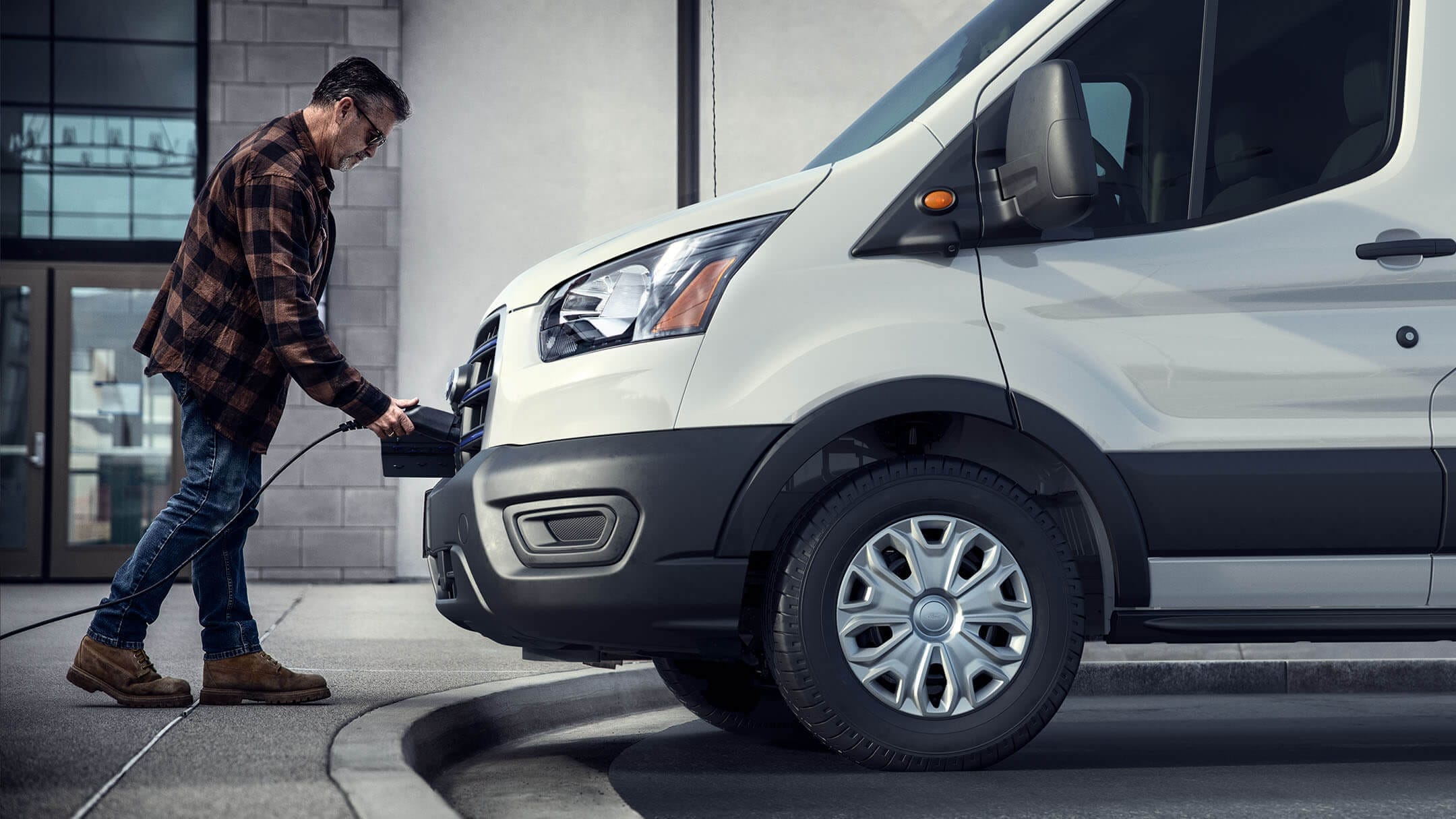 Ford E-Transit in Weiß. Seitenansicht, Mann lädt E-Transit auf