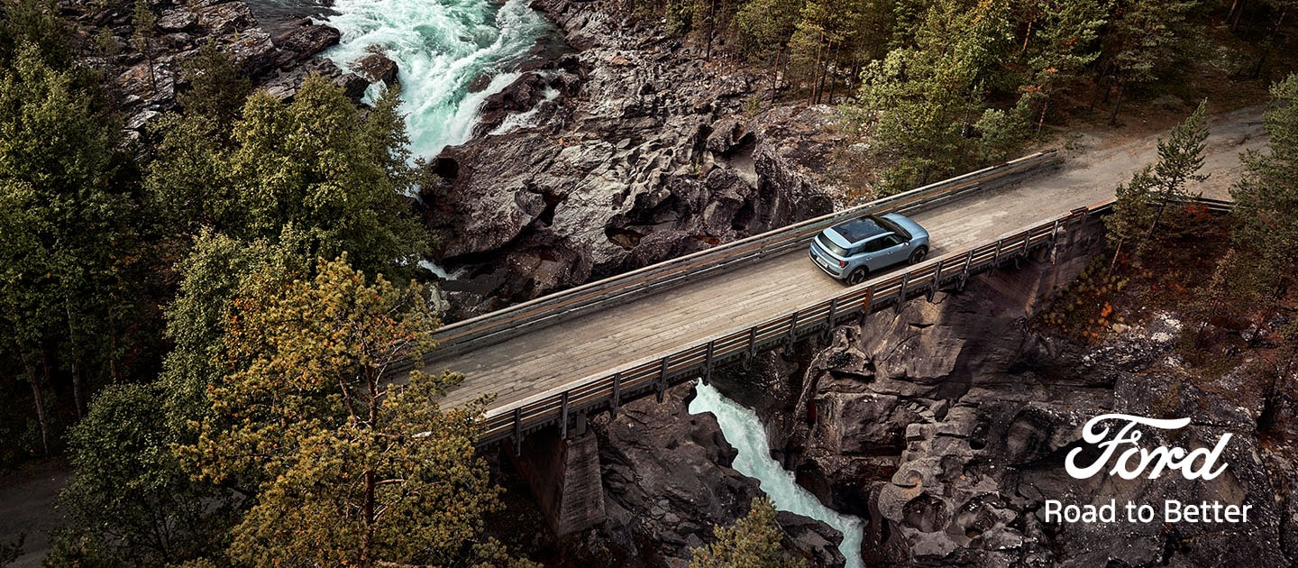 Der vollelektrische Ford Explorer in Blau. Ansicht von oben, fahrend über eine Brücke mit Wald im Hintergrund.