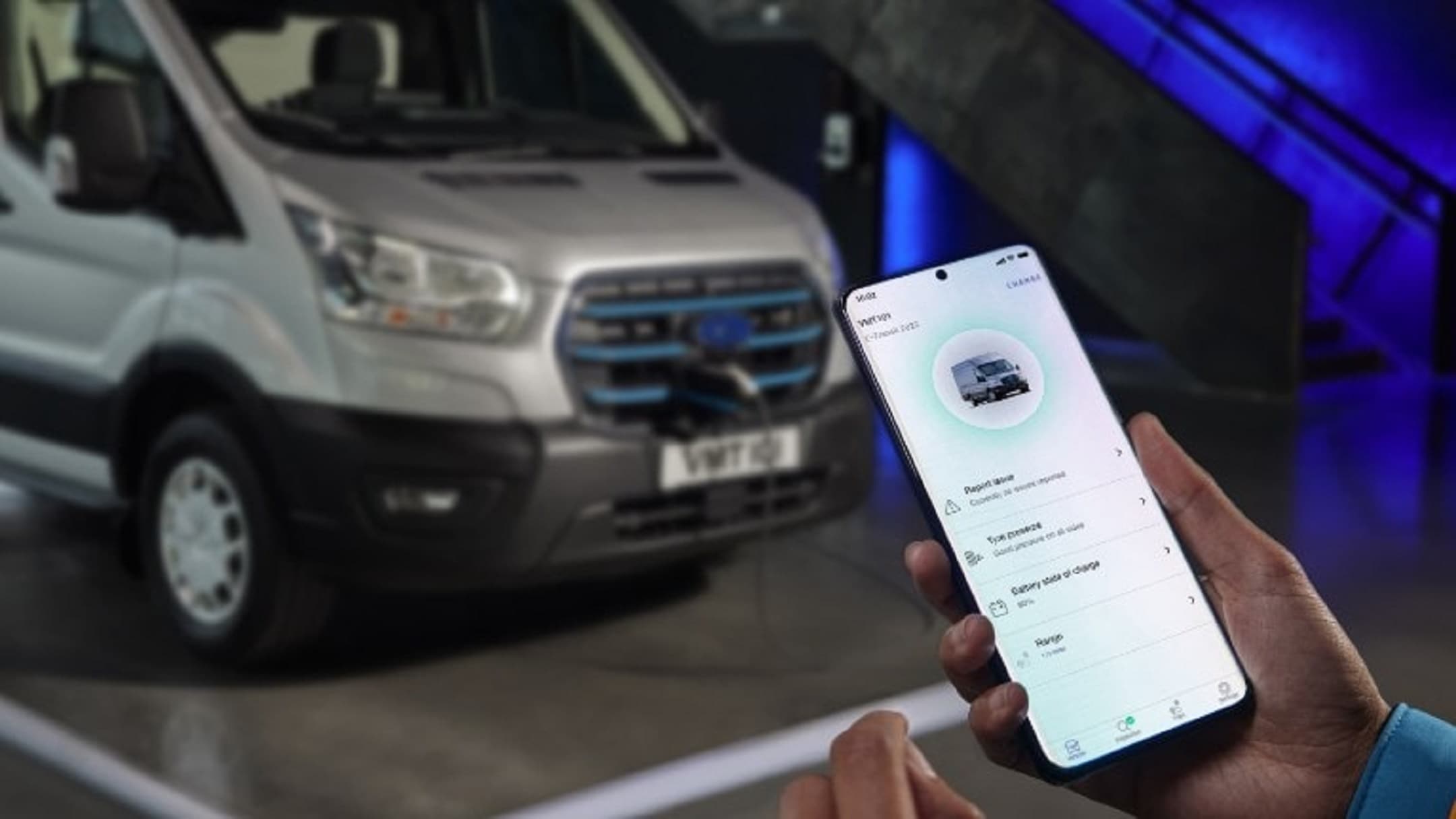  Ford E-Transit in Silber. Frontansicht, Hand hält Smartphone
