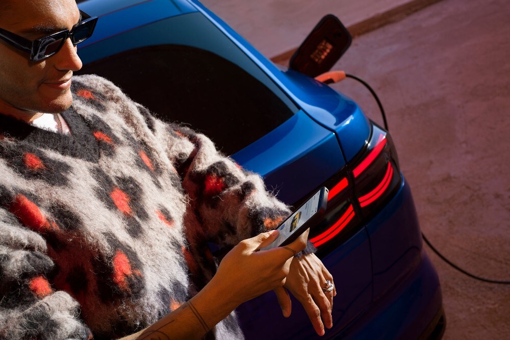 Mann lehnt an blauem E-Ford Capri, schaut auf Handy.