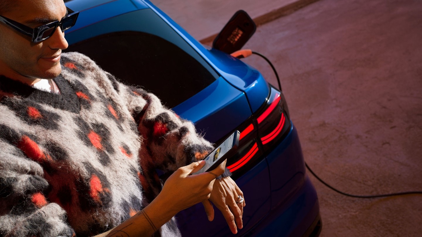 Mann lehnt an blauem E-Ford Capri, schaut auf Handy.
