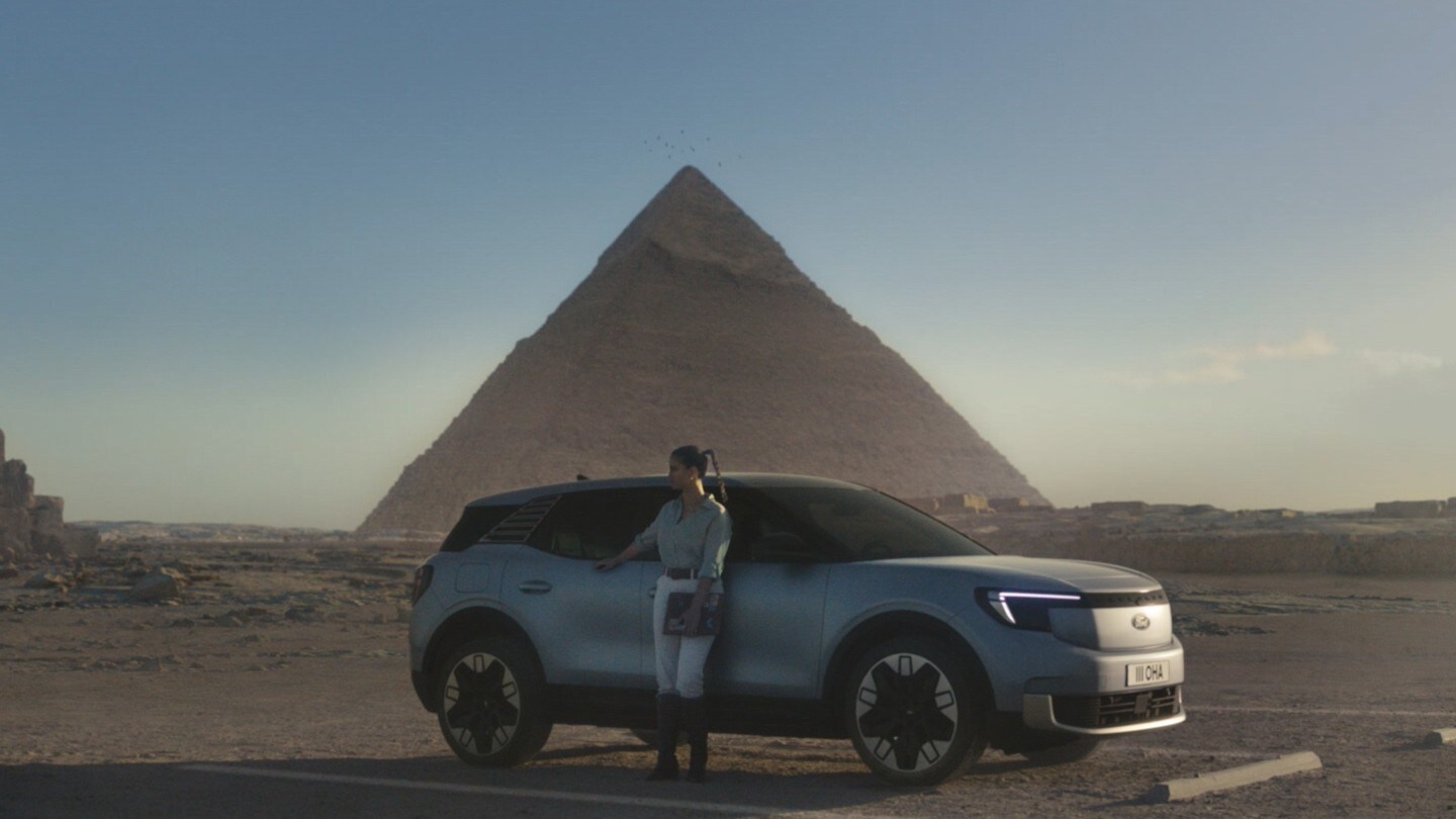 Lexie Limitless stehend vor dem neuen vollelektrischen Explorer mit einer Pyramide im Hintergrund. 