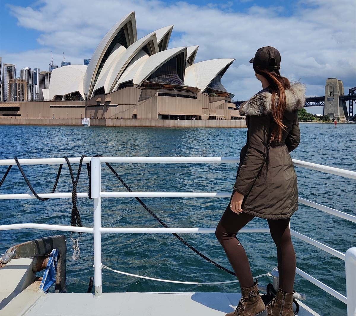 Lexie Limitless stehend am Schiffsgeländer mit Ausblick auf das Sydney Opera House.