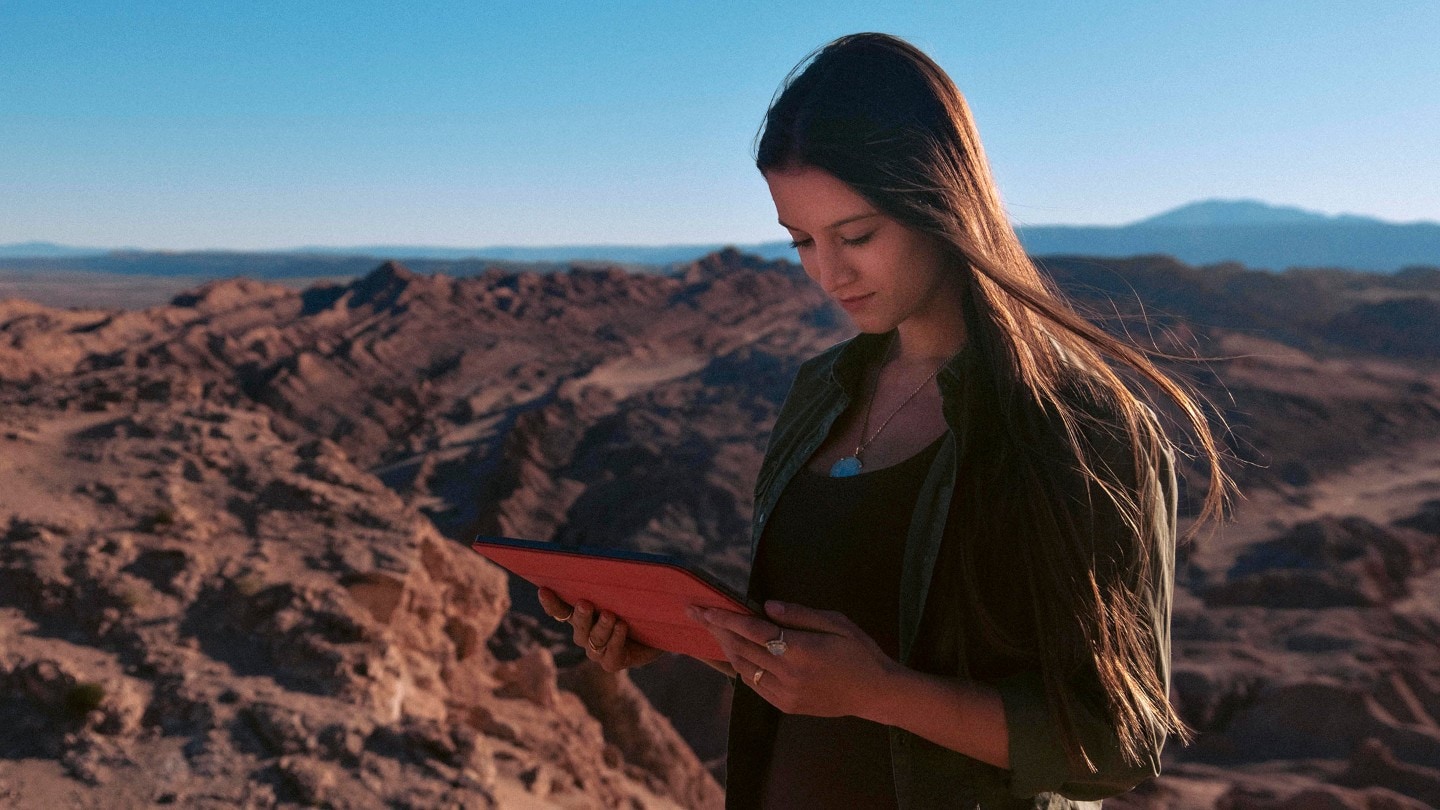 Lexie Alford steht in bergiger Landschaft und schaut auf ein Tablet