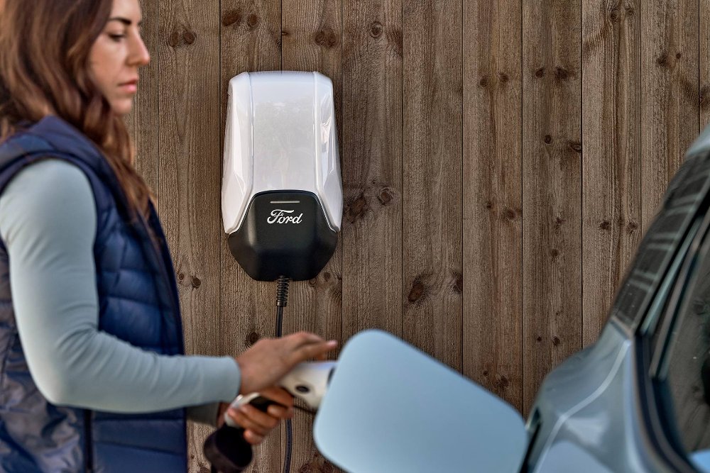 Eine Frau schließt einen blauen vollelektrischen Ford Explorer über ein Ladekabel an eine Wallbox für Elektroautos an." draggable="false" title="Eine Frau schließt einen blauen vollelektrischen Ford Explorer über ein Ladekabel an eine Wallbox für Elektroautos an.