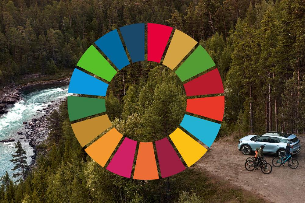 Blauer, vollelektrischer Ford Explorer, geparkt im Wald am Ufer eines Flusses. Zwei Mountainbiker neben dem Elektro SUV. Das Logo der UN-Nachhaltigkeitsziele ist eingeblendet.