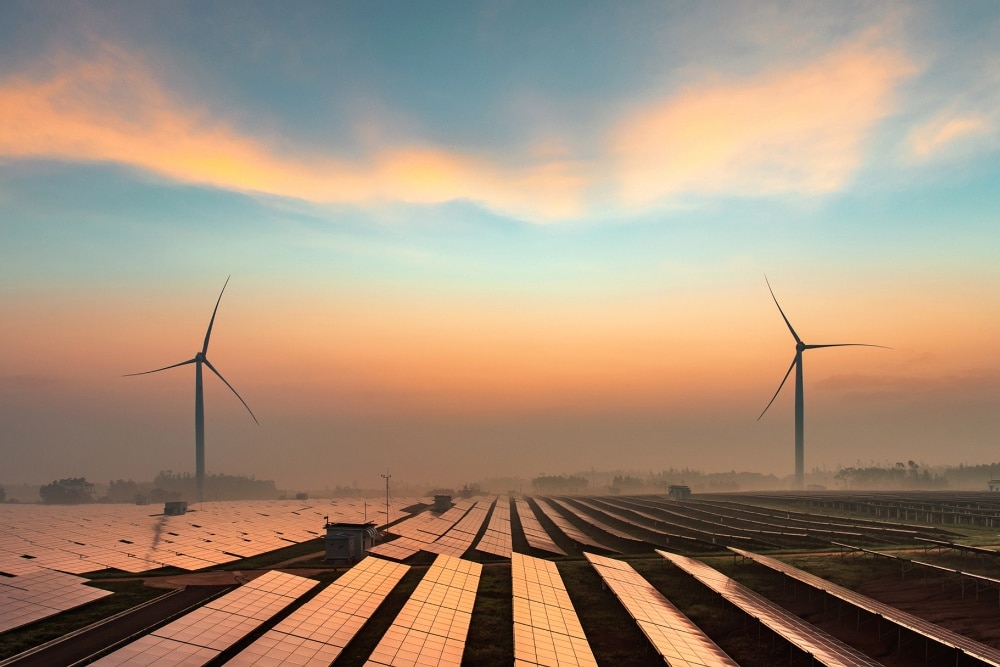 Ein Feld mit Photovoltaik Module und Windkrafträdern am Horizont bei Sonnenuntergang." draggable="false" title="Ein Feld mit Photovoltaik Module und Windkrafträdern am Horizont bei Sonnenuntergang.