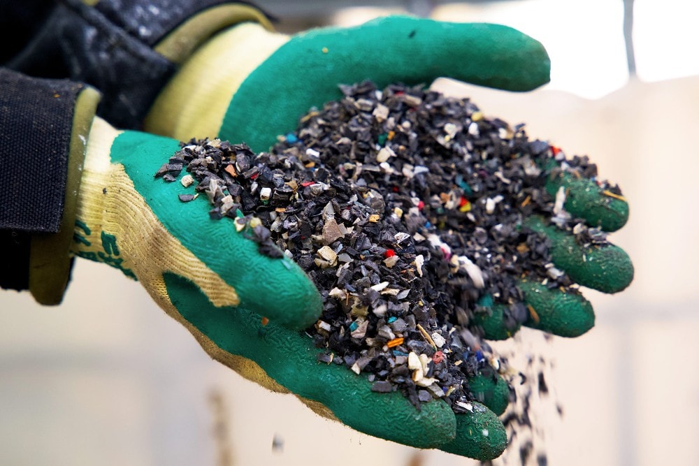 Zwei Hände mit Gummihandschuhen halten Stücke recycelten Kunststoffs.