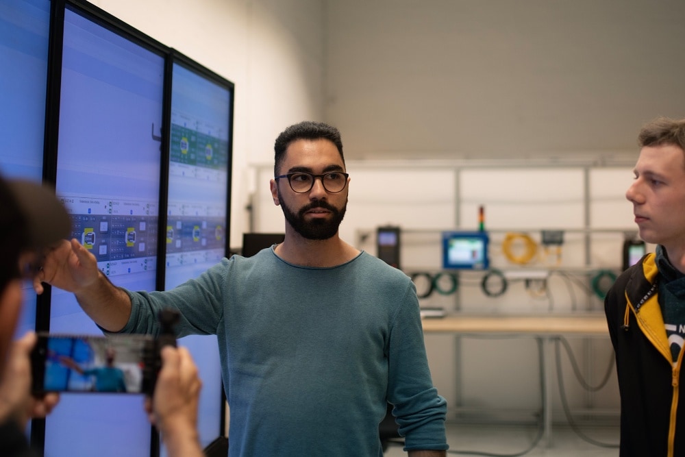 Ford Mitarbeiter bei einem Stand-Up Meeting. Eine Person erläutert seinem Team eine auf einem Bildschirm gezeigte Grafik." draggable="false" title="Ford Mitarbeiter bei einem Stand-Up Meeting. Eine Person erläutert seinem Team eine auf einem Bildschirm gezeigte Grafik.