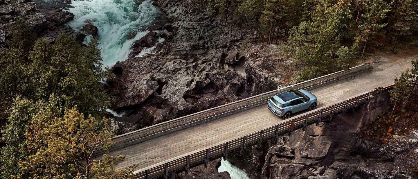 Vollelektrischer Ford Explorer in Blau. Vogelperspektive, fährt über eine schmale Holzbrücke über einen Fluss