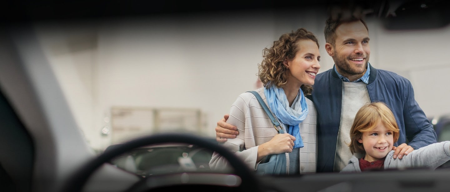 Eine Familie steht lächelnd vor einem Auto