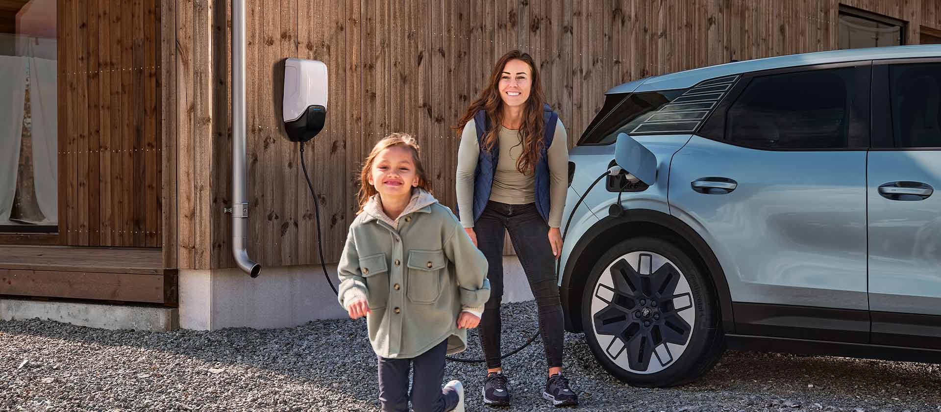 Ford Explorer in Blau. Seitenansicht, an ein Ladekabel angeschlossen. Frau und Kind im Vordergrund. 