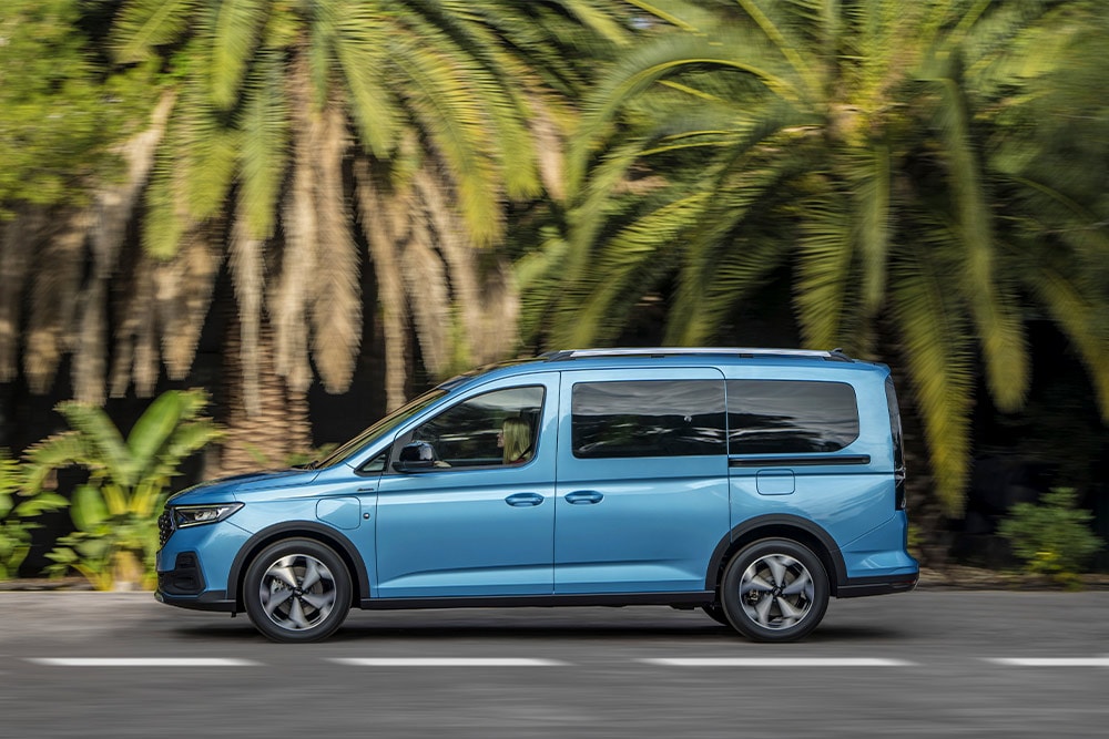 Ford Tourneo Connect in Blau. Seitenansicht, fahrend auf einer Straße. Palmen im Hintergrund.