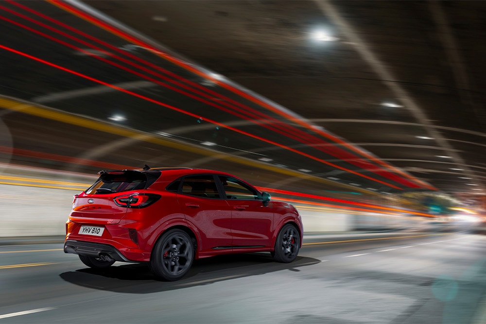 Ford Puma in Rot. Frontansicht, fahrend durch die Stadt bei Nacht.