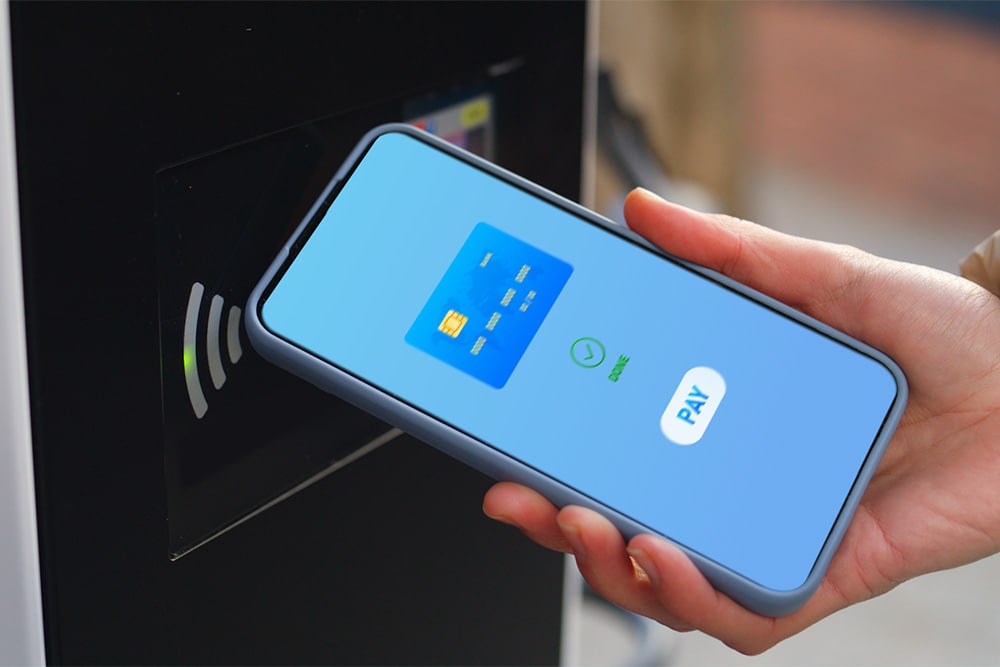 Eine Person verwendet kontaktlos ihr Smartphone, um an einer öffentlichen Ladestation zu bezahlen.