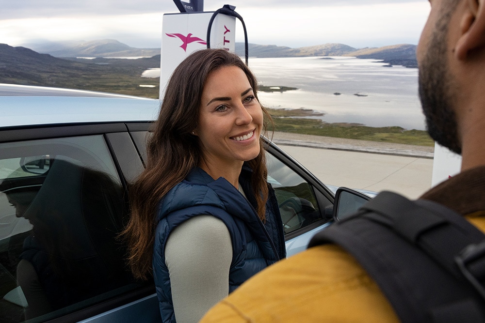 Zwei Personen stehen neben einem vollelektrischen blauen Ford Explorer, der an einer IONITY auflädt.
